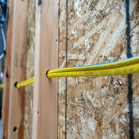 Yellow electrical wire passing through wood panel in indoor installation.