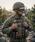 First aid kit pouch on black tactical MOLLE vest, front view, worn by camo-clad soldier outdoors