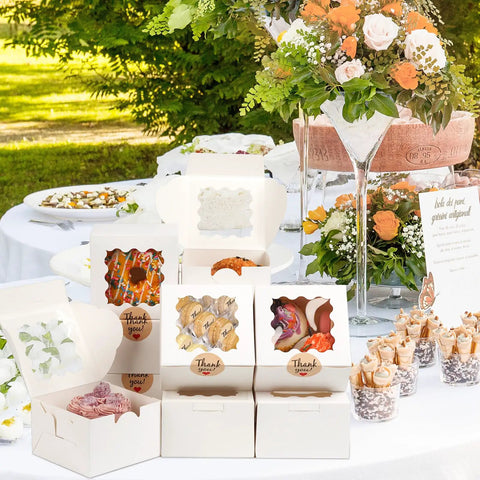 Premium White Cookie Boxes With Clear View Window And Included Thank You Labels 12 Pack 6x6x3 inches displayed at event.