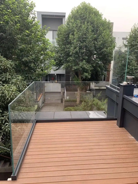 Heavy Duty Glass Railing System For Deck And Balcony Featuring Rock Solid Spigot Clamps With Flexible Floor Or Side Mount Hardware And Premium Aluminum Posts In Matte Black Covers For Quick Pool And Yard Fence Projects on a wooden deck.