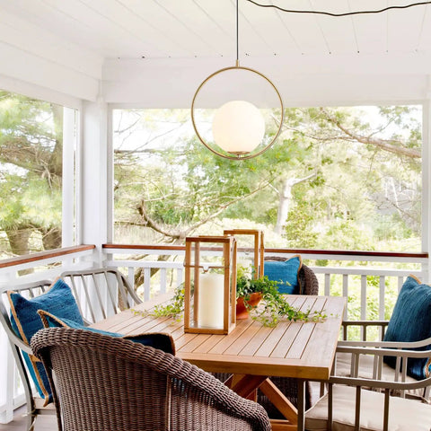 Modern mid-century style chandelier with white glass ball and brushed brass ring, hanging over a dining table on a porch.