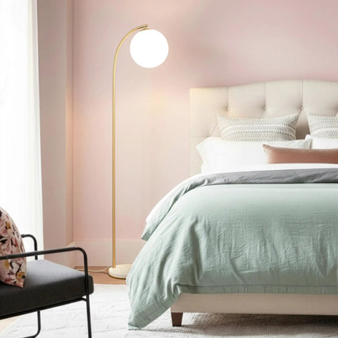 Luna Drop 75 Inch Antique Brass Floor Lamp With Frosted White Glass Globe Shade in a bedroom next to a bed