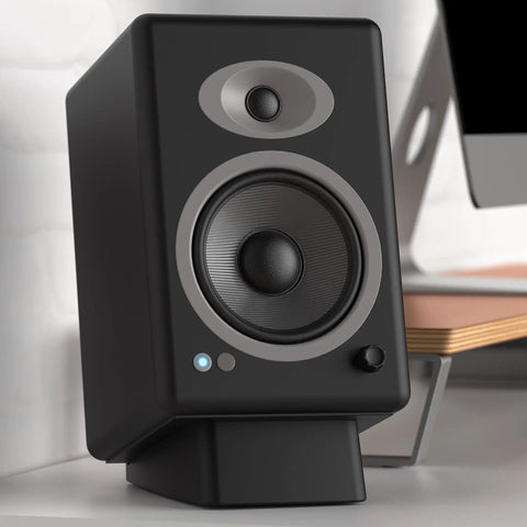 Black angled desktop speaker stands with anti slip silicone wedges for medium speakers, setup with monitor on desk.