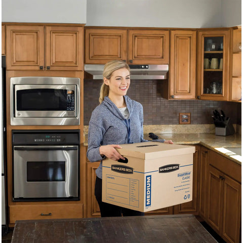 Person carrying Solid Gear Medium Moving Boxes 20 Pack With Tapeless Assembly And Reinforced Carry Handles in a kitchen.