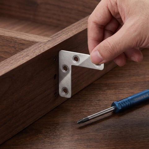 Person installing 100 Piece L Bracket Corner Brace Set, 2x2 Inch Stainless Steel Angle Joint Brackets on wooden furniture.