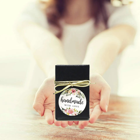 Black gift box with 'handmade with love' floral label on wooden table, presented by hands
