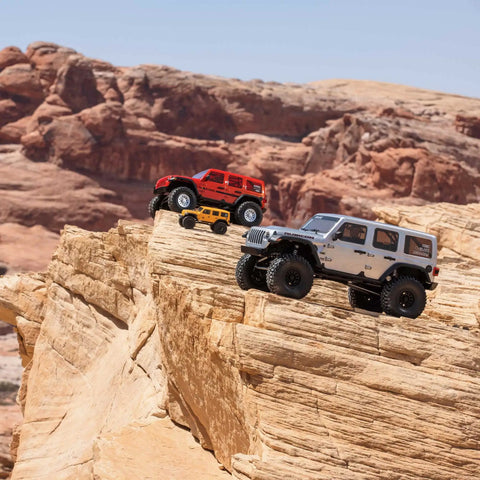 One Sixth Scale SCX6 Jeep Wrangler 4x4 Rock Crawler RTR with Two Speed Transmission on rugged cliff, silver and red models