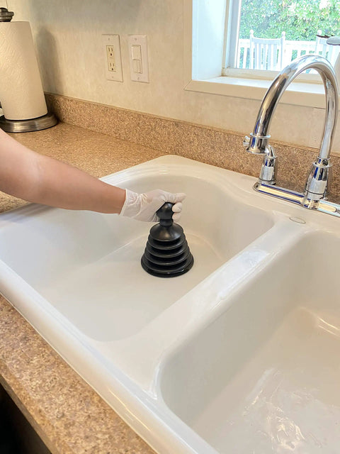 Hand using Mighty Tiny Plunger For Tight Spaces And Small Drains, Perfect For Bathroom And Kitchen Sinks, RVs And More, Patent Pending Black in a kitchen sink.