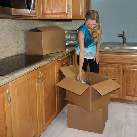 Woman packing kitchen items into Heavy Duty Corrugated Moving Boxes For No Drama Packing Medium 18X14X12 Inches Brown Cardboard Cartons.