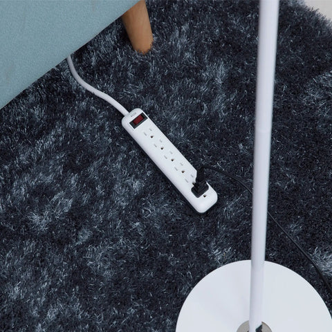 Six-Outlet Power Strip 3-Pack With Overload Protection And 3-Foot Cord White Back-Mount Holes For Easy Desk Setup 15A 125V 60Hz Durable Home Office Extension on carpet next to a sofa and lamp.