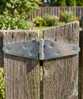 Close-up of a silver T strap hinge attached to weathered wooden gates, showcasing the Set Of 6 Heavy Duty 4 Inch Silver T Strap Hinges For Barn Gates And Exterior Doors Premium Steel Build With Mounting Screws.