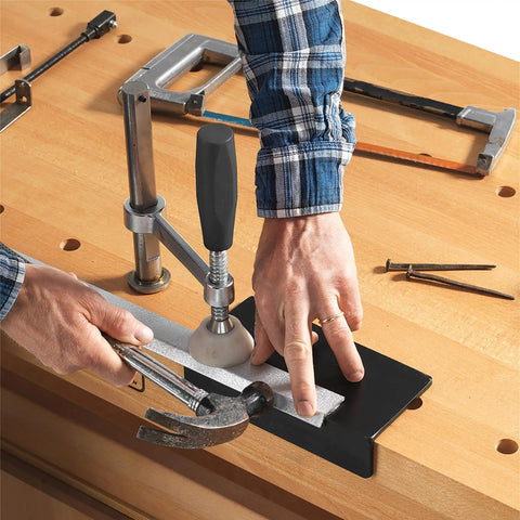 Hands using Badass Workbench Accessory Kit with steel anvil and vise pads on a wooden workbench for optimal grip and stability.