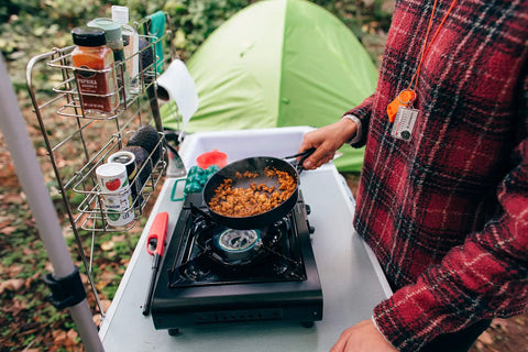 Cooking on portable outdoor butane stove for camping and catering with electronic ignition, single burner, black in use, tent nearby.