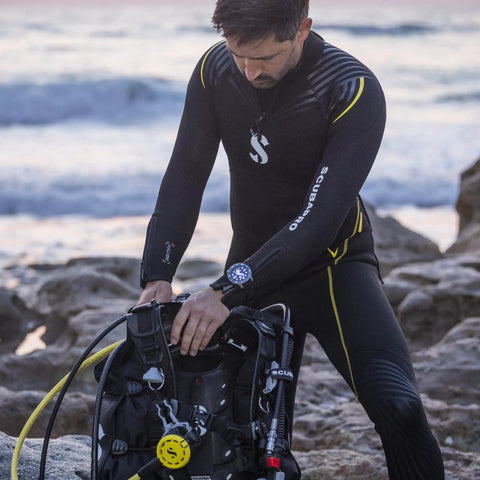 Diver wearing Dope Titanium Dive Wrist Computer With Wireless Transmitter handling scuba gear on rocky shoreline.