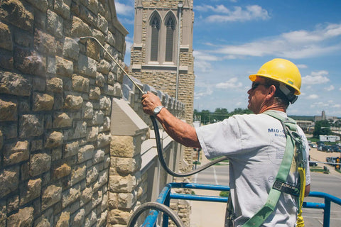 Worker applying The Real Deal Deep Penetrating Siloxane Masonry Sealer For Brick Concrete And Stucco on a stone wall.