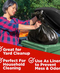 Person placing 65 Gallon Heavy Duty Trash Bags 50x60 Inches Extra Large Black Contractor Liners in green outdoor can