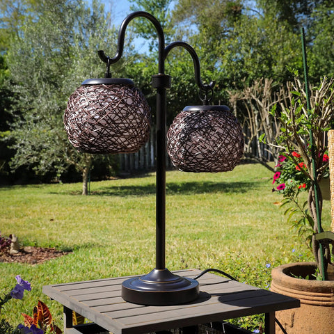 Castillo Outdoor Table Lamp In Oil Rubbed Bronze With Woven Rattan Shades in a garden setting, rustic two-light patio lamp.
