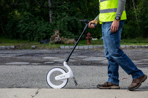 Rock Solid Digital Measuring Wheel And Smart Mapping Kit With Sprayer Attachment And Heavy Duty Carrying Case in use on pavement.