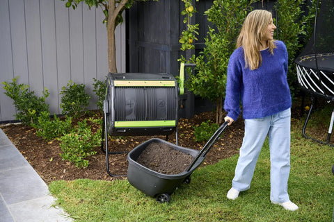 Woman using 48 Gallon Geared Dual Chamber Compost Tumbler with Large Fill Openings Elevated Design to fit compost cart