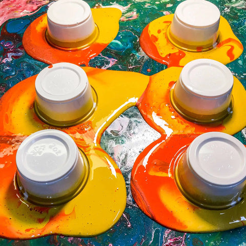 Colorful paint pouring over plastic cups demonstrating Floetrol Additive For Latex And Acrylic Paints To Improve Flow And Brushability