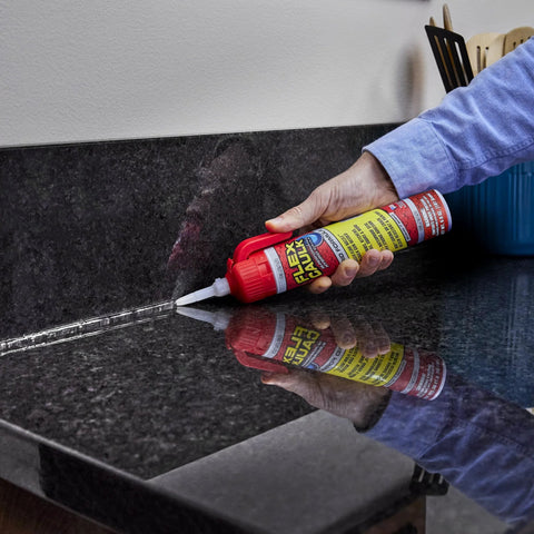 Hand applying Flex Caulk sealant from red-capped tube to black granite countertop seam.