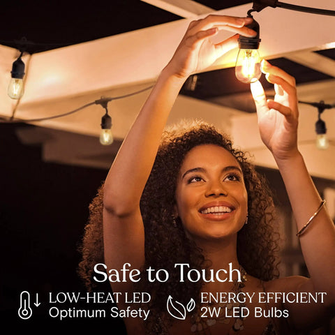 Woman installing Ambience Pro Waterproof LED Outdoor String Lights for Patio 48 Ft With 15 Hanging Dimmable 2W Vintage Edison Bulbs