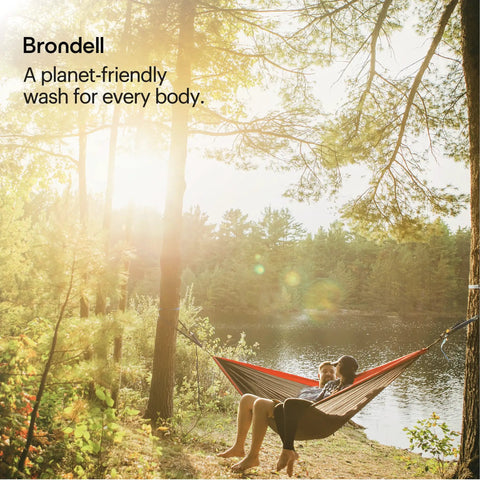 Person relaxing in a hammock near a lake surrounded by trees with text 'Brondell: A planet-friendly wash for every body'