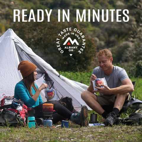Two backpackers enjoying Gluten Free Korean Inspired Beef Freeze Dried Trail Ready Camping Meal For Backpackers next to their tent.