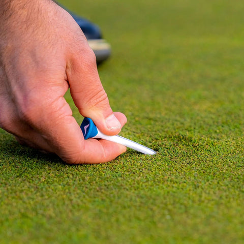 Hand placing a Premium Slick Rubberized Golf Tee With Durable Plastic Base For Low Spin Launch Assorted Colors 4 Pack into grass.