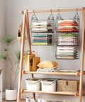 Five Tier Closet Hanging Organizer With Four Sturdy Hooks For Clothes Sweaters Shoes Handbags And Purses Zero Hassle Wire Storage Bins hung with colorful folded clothes on a wooden rack.