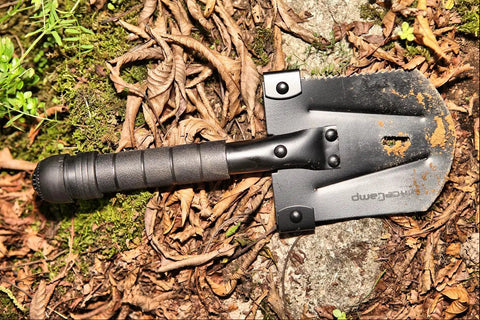 Grab-N-Go 12-In-1 Survival Multi-Tool Shovel for Camping and Outdoor Adventures on forest floor with soil on blade