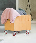 Wooden box with blankets on heavy duty swivel and rigid caster wheels with brakes, showing polyurethane casters and steel bracket design.
